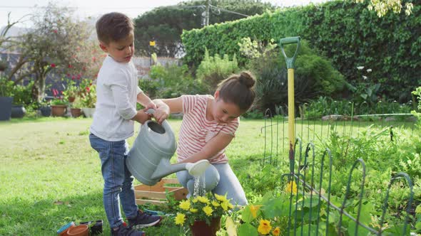 Happy caucasian siblings gardening, watering flowers together