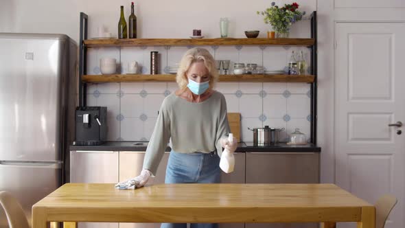 Mature Housewife in Safety Mask Disinfect Kitchen Table