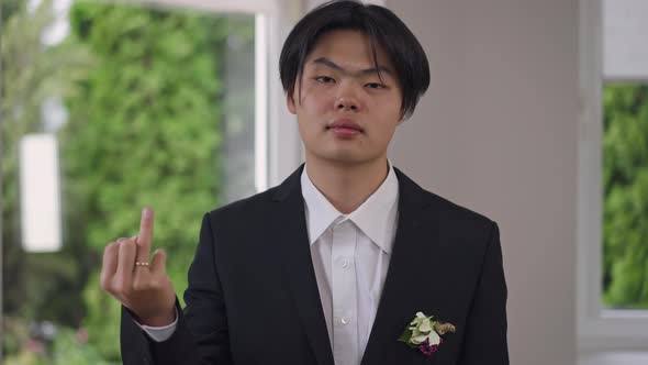 Portrait of Confident Asian Groom in Elegant Suit Showing Finger with Wedding Ring Looking at Camera