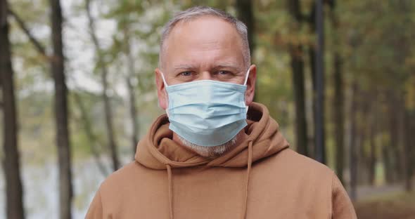 Portrait of Elderly Man, Adult Man Removes a Protective Medical Mask and Looks at the Camera, Gray