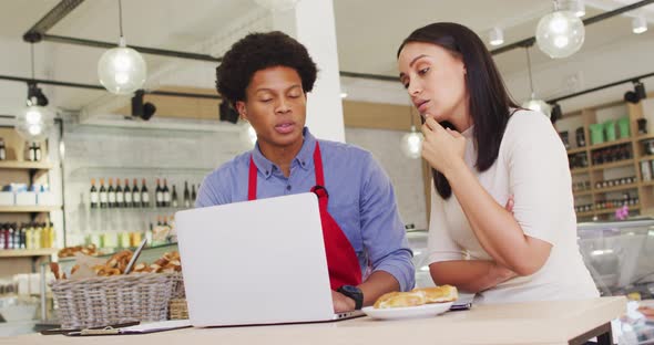 Video of diverse female owner and male waiter working with laptop at cafe shop