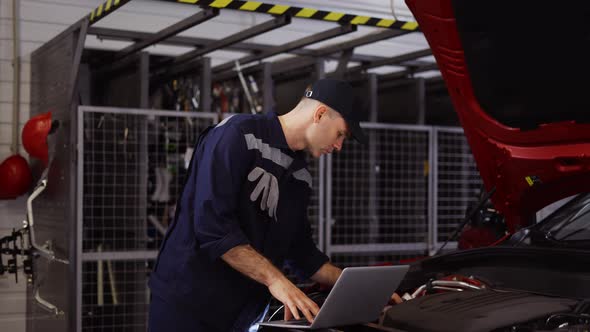 Auto Mechanic Uses a Laptop While Conducting Diagnostics Test on Engine