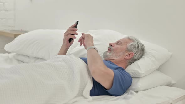 Old Man Using Smartphone While Lying in Bed