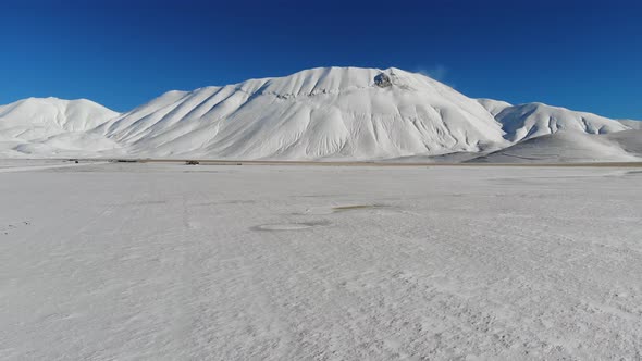 Drone flight over frozen landscape towards Piano Grande, Castelluccio