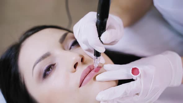 A beautician gently applies a pink hue pigment to the client’s lips