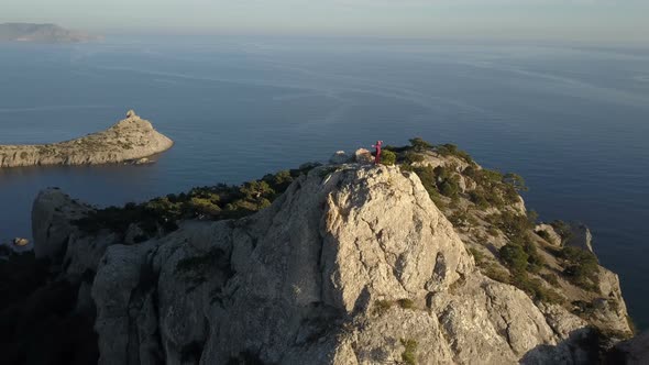 Aerial View of a Young Woman Standing on the Top of a Mountain Facing the Sea. Lady on the Summit in