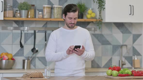 Young Man Using Smartphone While Standing in Kitchen