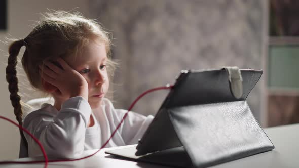 Bored Girl Watches Educative Video Via Tablet at Table