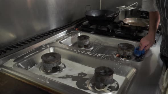 Man cleaning the gas hob in a restaurant kitchen