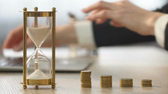 Business Lady Working on Laptop and Adding Coin to Stack of Money, Economics