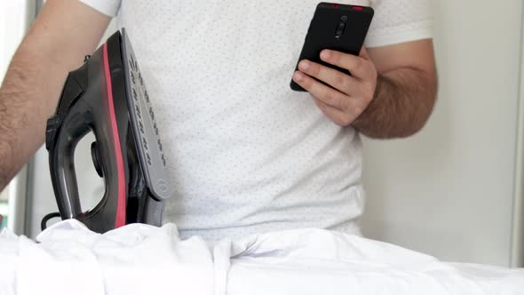 man forgets to stand up iron from white shirt and is playing,using mobile phone.busy man chatting,so