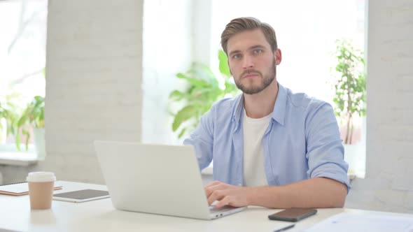 Creative Man Looking at Camera While Using Laptop in Modern Office