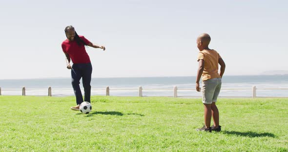 Video of happy african american father and son playing soccer outdoors and having fun