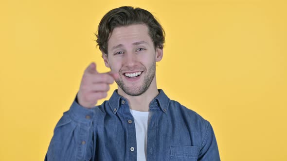 Young Man Pointing at Camera in Approval on Yellow Background