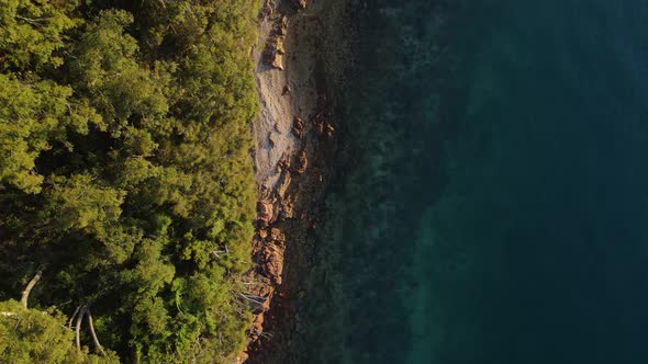 High revealing view of a rugged coastal headland next to tropical blue swimming area. Drone view loo