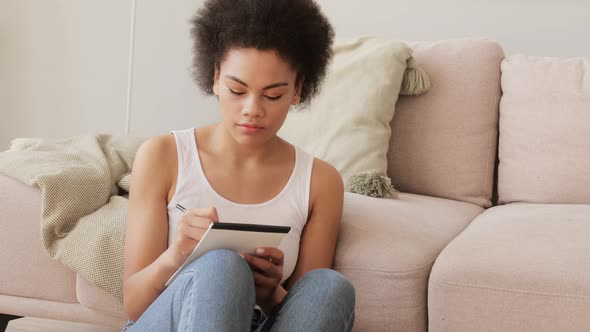 Young african american inspired woman pensively thinks and making notes in paper notebook.