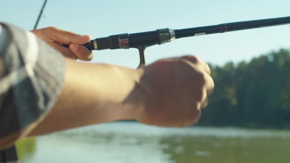 Closeup of Black Fisherman Holding Fishing Rod and Turning Reel By Lake