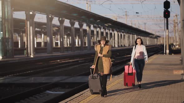 Two Girls at the Railway Station with Their Suitcases Out on the Platform Waiting for the Train