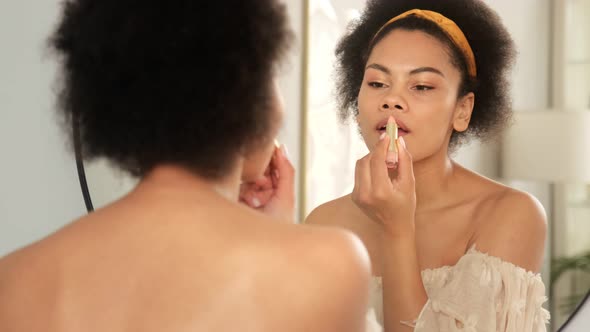 African american woman doing make up, holding lipstick and paints lips.