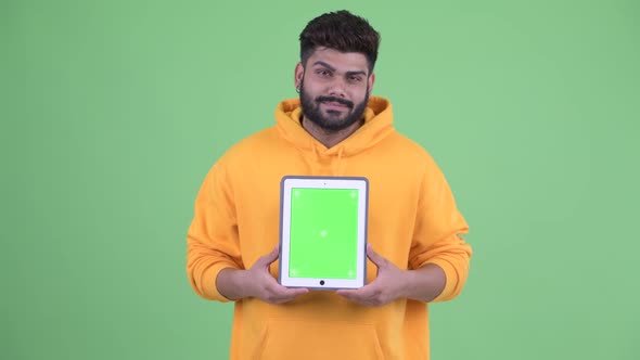 Happy Young Overweight Bearded Indian Man Thinking While Showing Digital Tablet