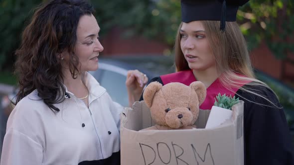 Worried Graduate Woman with Dorm Room Box and Mature Mother Supporting Grad Daughter Standing