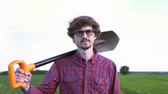 The farmer holds a shovel in his hand on an agricultural field, harvest time.