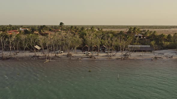 Offroad vehicles on Guriu beach through village in sunset glow; drone profile