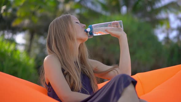 Superslowmotion Shot of a Young Woman on a Tropical Beach Sits on an Inflatable Sofa and Drinks