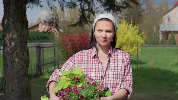 The Girl Carries Flowers in Her Hands to Plant Them in the Garden