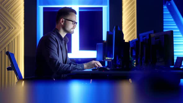 A Man with Glasses Sits and Thinks Typing on a Computer in the Office at Night