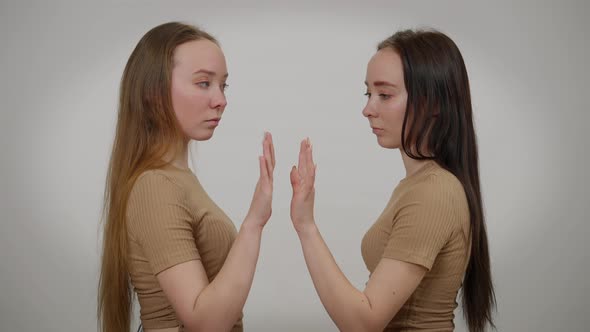 Identical Twin Sisters with Red and Black Hair Imitating Touching Glass Standing at Grey Background