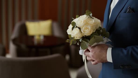 Man in Blue Suit Walks Into Hotel Holding Bouquet of Roses in Front of Him