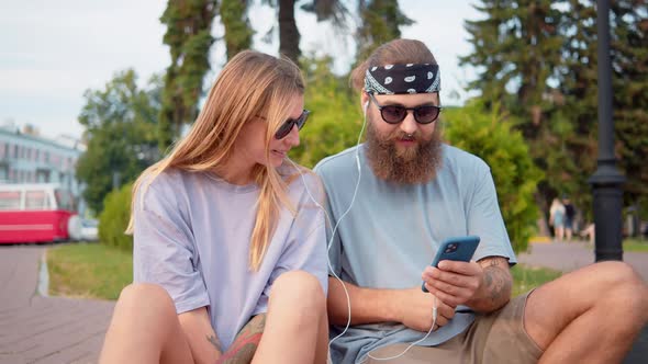 Young Cheerful Man and Women Looking a Phone Screen Put Headphones in Ears