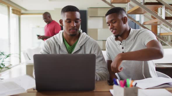 Two african american teenage twin brothers using a laptop and talking with father in background