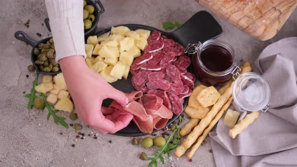 Making Meat and Cheese Antipasto Plater Woman Putting Pieces of Prosciutto Ham on Stone Serving