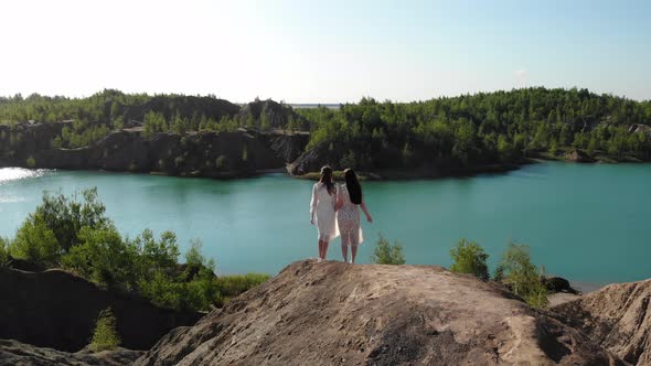 Incredible View of Two Women on Top of Mountain Against Background of Blue Lake on the Edge Hold