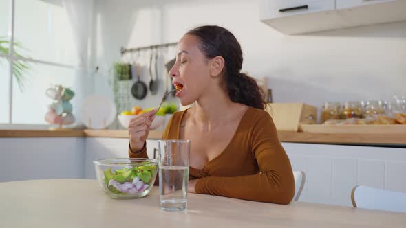 Young happy attractive Latino woman eat green salad in kitchen for health care wellness at home.