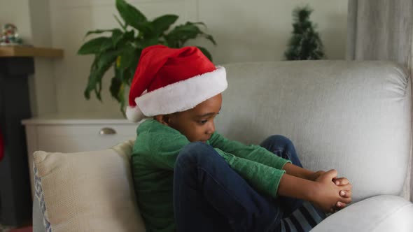 Animation of sad african american boy wearing santa hat sitting on sofa at christmas time