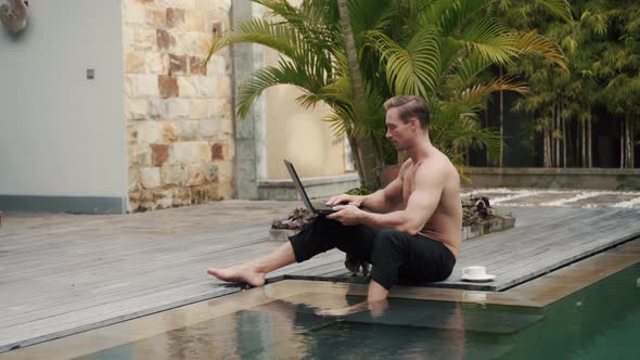 Sporty Caucasian Topless Man Works on Vacation Outdoor at the Pool with Laptop