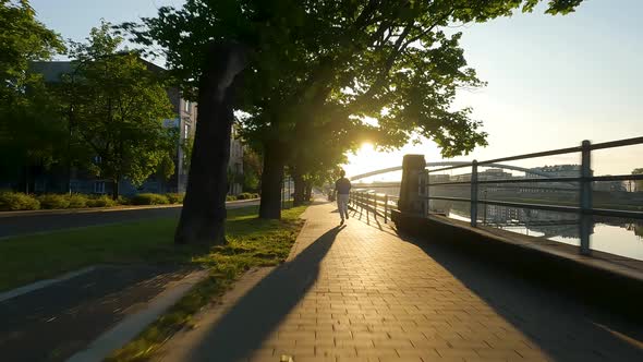 Woman is Jogging Along the Embankment at Sunrise