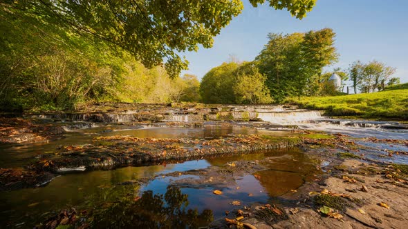 Panorama time lapse of spring forest cascade waterfall surrounded by trees with rocks in the foregro