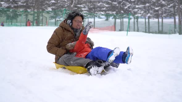 Asian Father And His Son Playing Sled Together