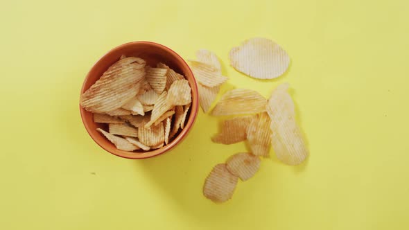 Close up of potato chips falling in a bowl with copy space on yellow surface
