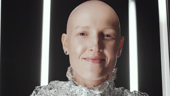 Young Bald Woman in Foil Wear Laughing at Camera in Dark Studio