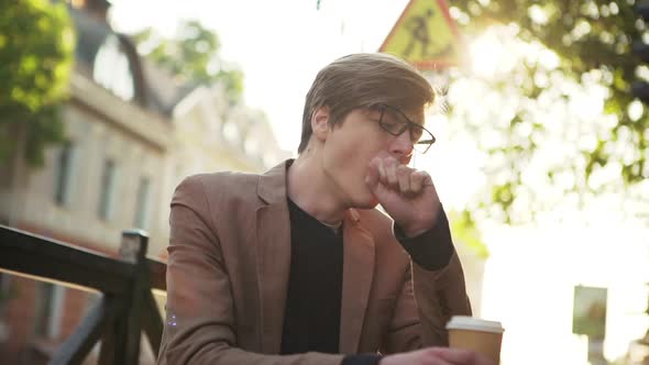 Handsome Sleepy Young Man Yawning Sitting Outside Cafe in Elegant Beige Jacket Early in Morning Slow