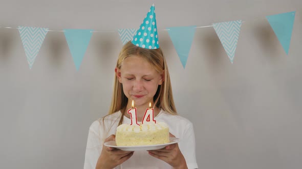 Cute Girl with Closed Eyes Making a Wish and Blowing Out the Candles Number Fourteen on a Birthday