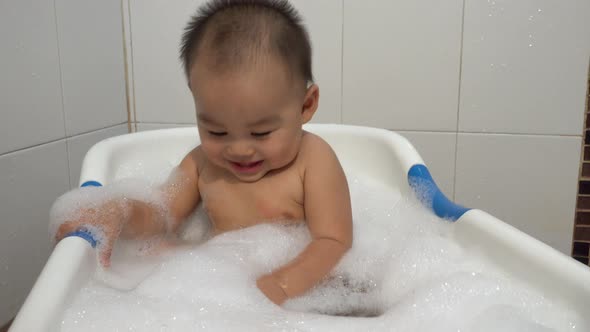 Little child funny take shower with soap suds in bath room interior at home