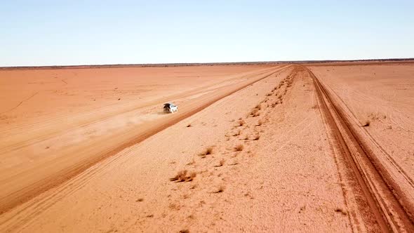 Drone following car with large dust trail as it travels on a desolate, open and flat dirt road.