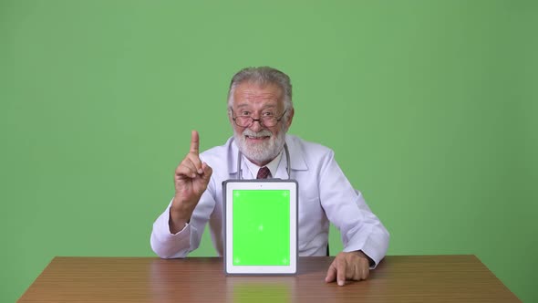 Handsome Senior Bearded Man Doctor Against Green Background