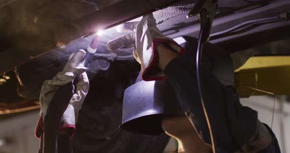 Female mechanic wearing welding helmet welding under a car at a car service station